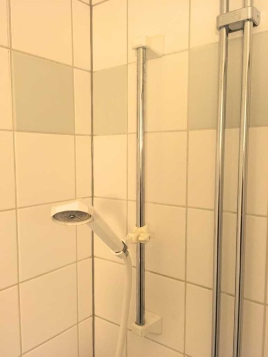 Duschhuvud och slang fäst vid en vertikal stång med justerbar hållare i ett kaklat badrum.