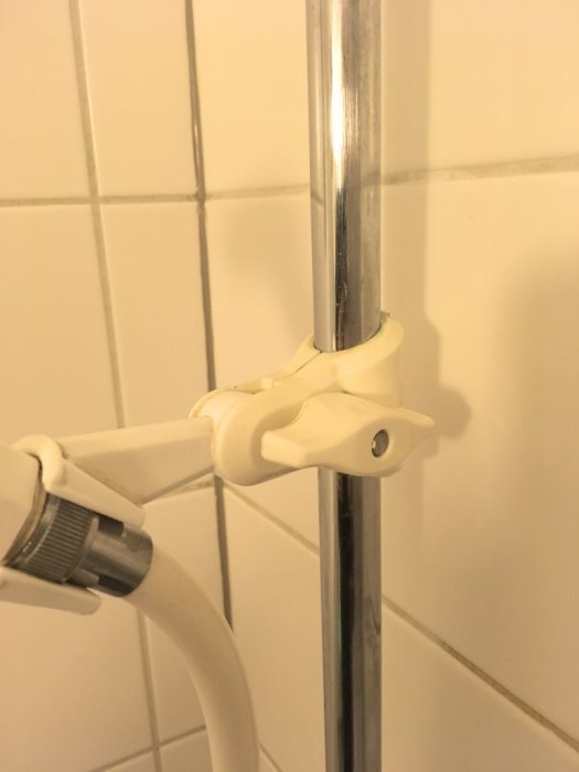 Justerbar duschmunstyckshållare i vit plast på en silverfärgad metallstång i en kaklad dusch.