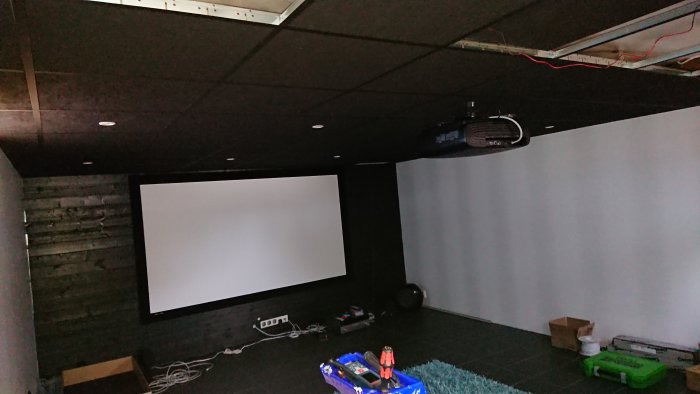 Hembiograf med stor projektorduk, projektor i taket och oavslutad inredning.