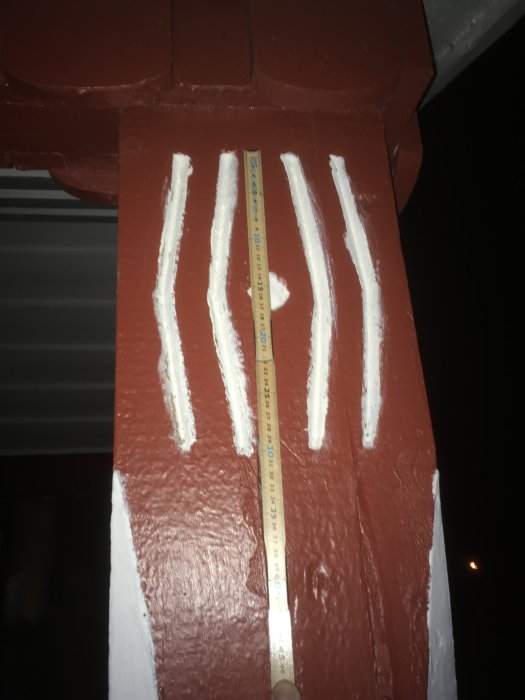 En röd husstolpe med vita utkarvade linjer som liknar en signatur, mätt med en tumstock.
