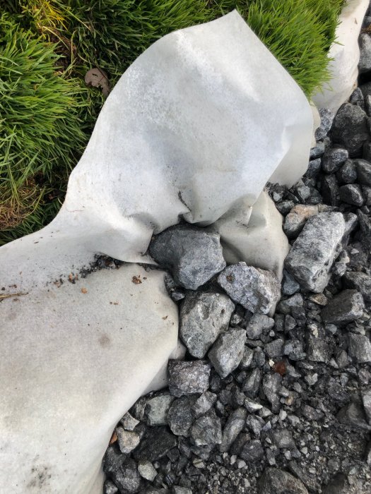 Markduk delvis täckt av makadam, vid gräskant, använd för underlag på åker.