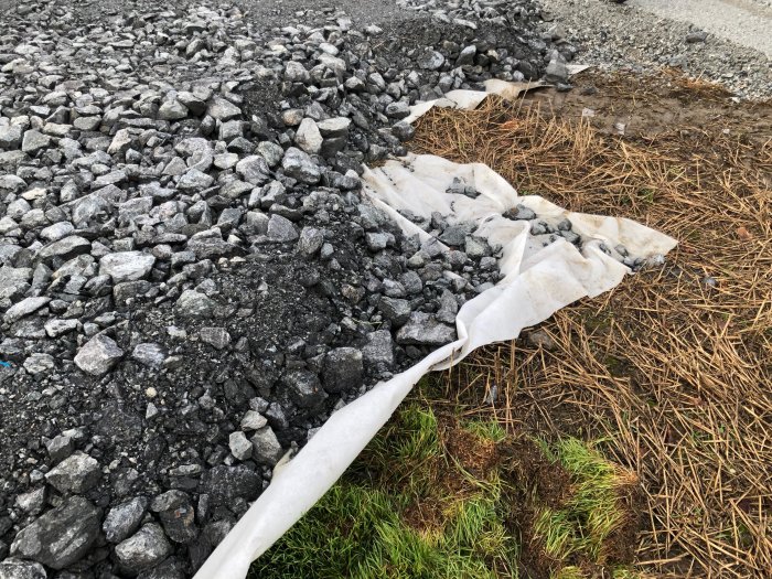 Markduk delvis täckt av grus och stenar nära en gräsmatta vid renoveringsarbete.