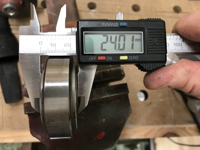 Skjutmått visar mätning på 24.01 mm på en maskindel i en verkstad.