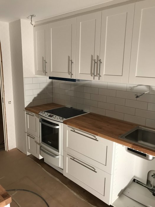 Kök under renovering med nya vita lådor, handtag och nyligen målad spis.