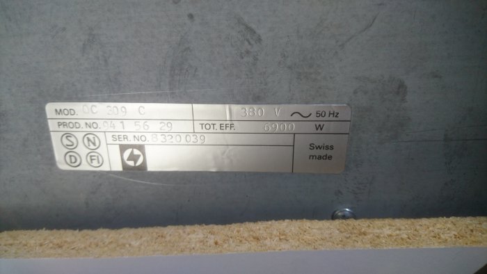 Märkskylt på en spishäll som visar modell, produkt- och serienummer samt total effekt på 6900 watt, Swiss made.