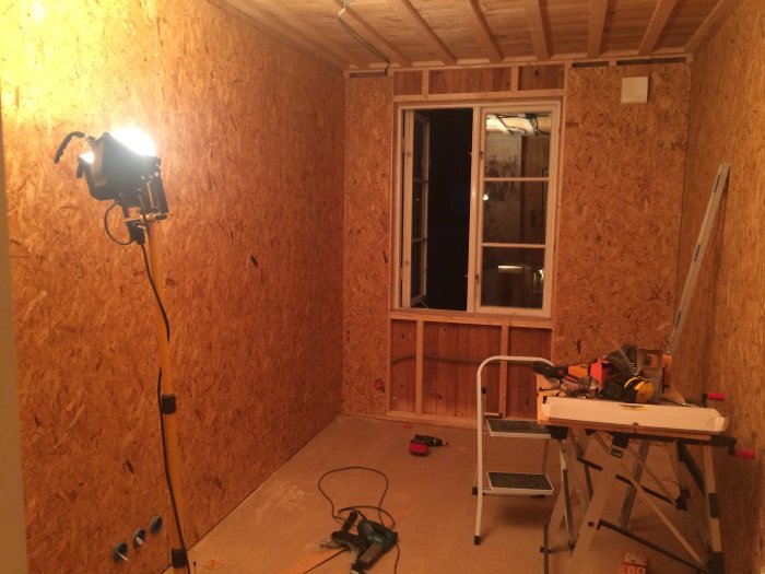 Byggarbetsplats med osb-väggar, elinstallationer och byggverktyg i ett rum under renovering.