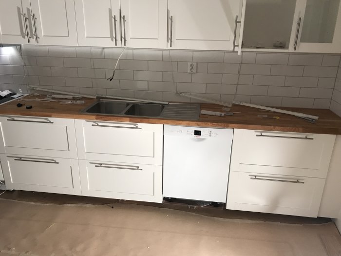 Kök under renovering med uppsatta vita lådor, handtag och bänkskiva, verktyg på bänken, ej färdigställd belysning.