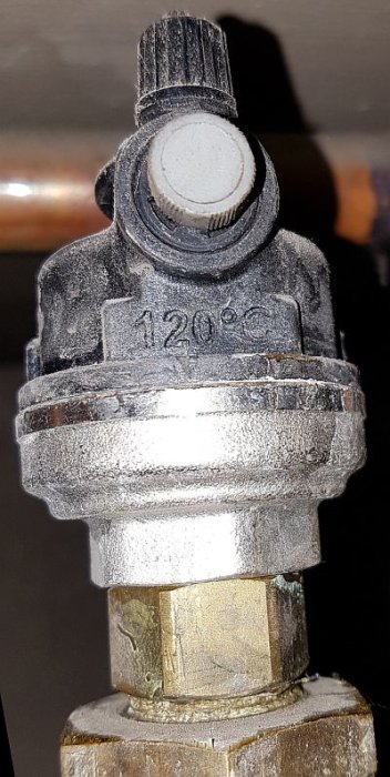 Närbild av en rörkoppling med ventilmekanism, märkt med 120°C, monterad på ett lodrätt rör.