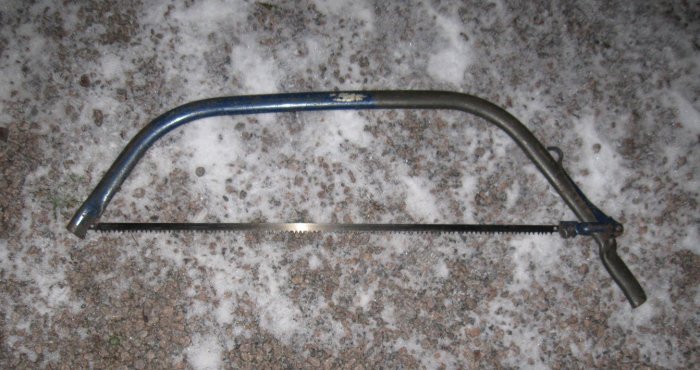 En traditionell purmobåge för sågning med 36 tums blad, liggande på ett grusigt och snötäckt underlag.