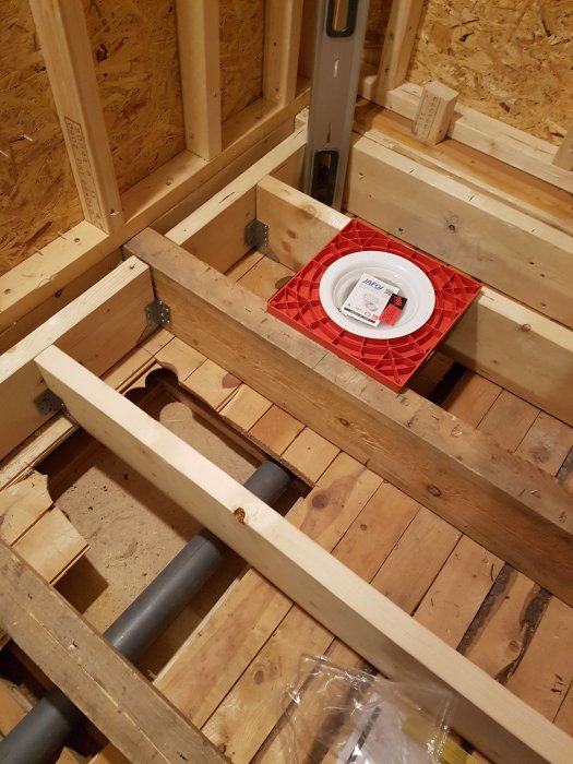 Golvbjälklag under konstruktion med en synlig röd ventilationshuv och en bärande bjälke redo för genomföring.