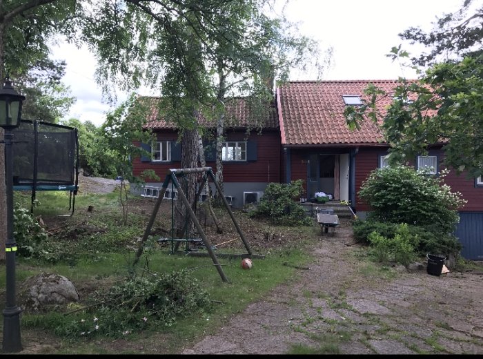 Rödmålat trähus med grå betongsockel och takkupa, trädgård med gungställning framför.