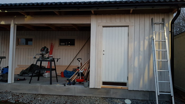 Garage under renovering med nyinstallerad förrådsdörr, kapmaskin och byggmaterial på golvet.