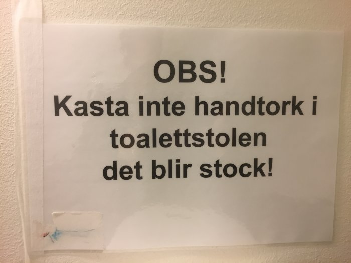 Varningsskylt med texten "OBS! Kasta inte handtork i toalettstolen det blir stock!" på en vägg.