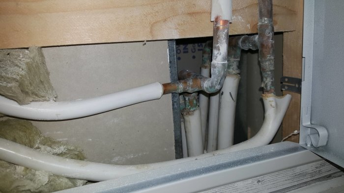 Komplex rörledning inuti en vägg med koppar och plastledningar samt isolering och en elcentral till höger.
