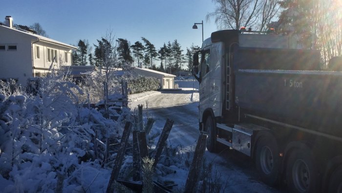 Snötäckt byggtomt med lastbil och snöklädda träd i soligt väder.