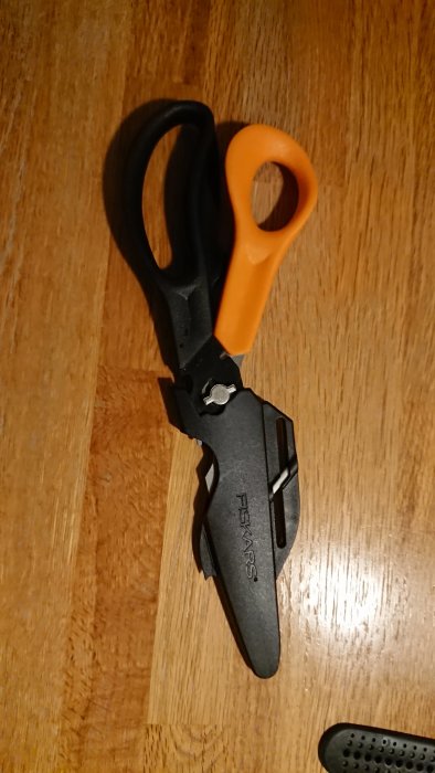 Fiskars actionsax med svarta blad och orange handtag ligger på ett träbord.