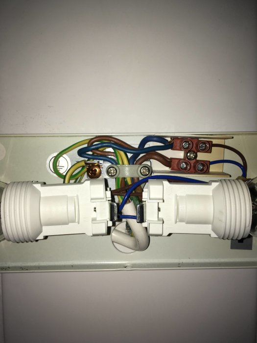 Elanslutningar skarvade i badrumsarmatur med öppen plint och synlig vit ledning till taklampa.