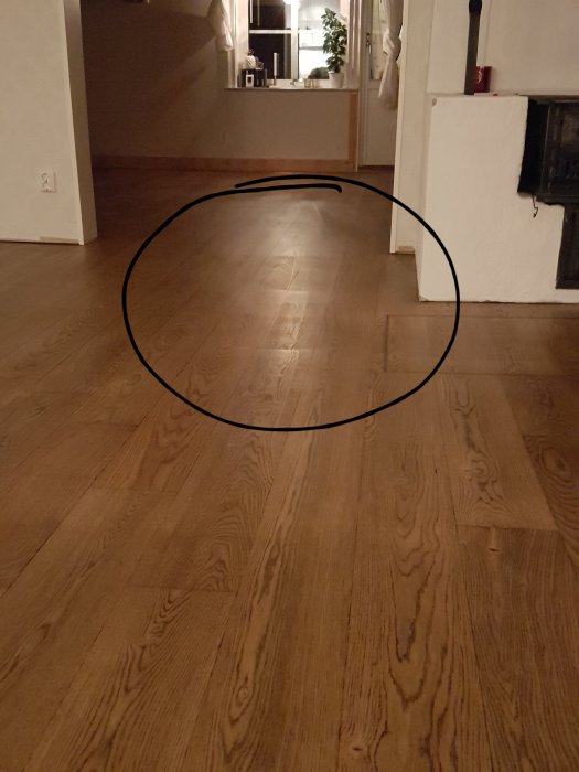 Ekparkettgolv med ojämn vaxbehandling som syns i vissa ljus, markerat med en cirkel.