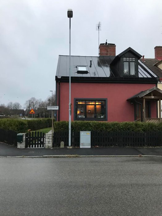 Rött hus med svart tak och solpaneler, vy från gatan mot entrén.