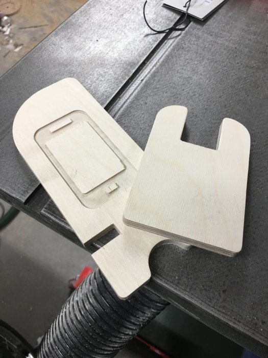 Obehandlad mobilhållare i björkplywood på en arbetsyta, tillverkad med CNC-maskin.