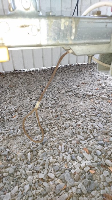 En rostig kabel hänger från en utrustningsdel mot en grushög.