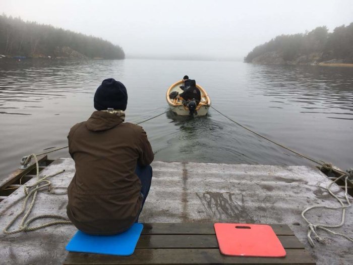 Person på brygga ser på båt som lämnar dimmigt öområde för pendling.