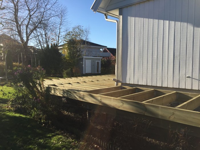 Uppbyggt bjälklag för badtunna i trädgården, med träbärlinor och balkskor synliga, intill ett vitt hus.