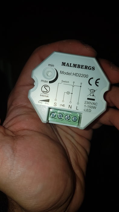 Hand håller en Malmbergs dimmermodul modell HD2200 med synliga anslutningsterminaler och instruktioner.