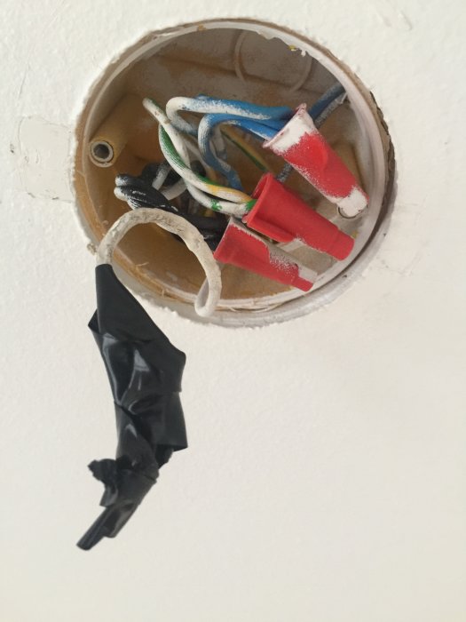 Elanslutning i tak med borttagen dosa, synliga kablar och isolertejp på en vit kabel.