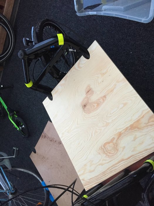 Träplywoodplatta på golvet förberedd för urtag med hjälp av CAD-modell, omgiven av cyklar och verktyg.