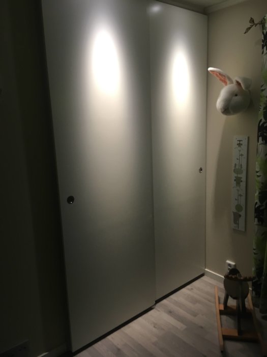 Skjutdörrar och dörrstopp monterade i en hemmiljö med leksaker och en väggprydnad föreställande ett djurhuvud.