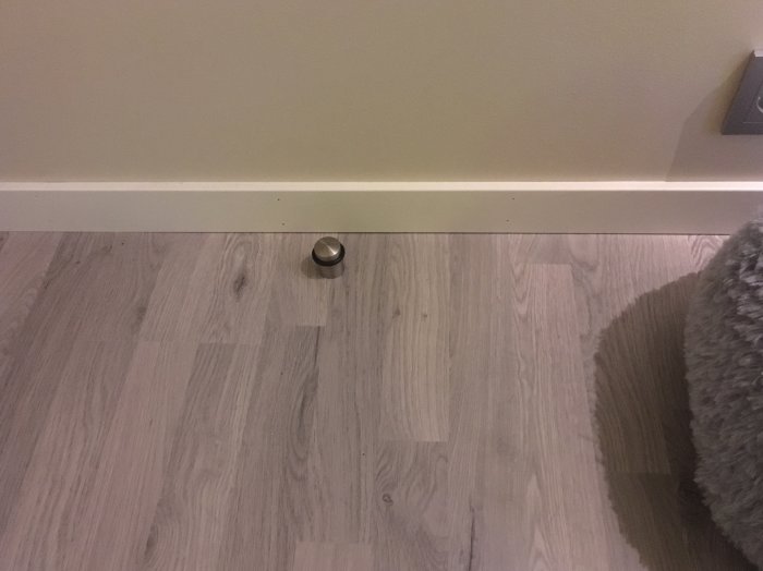 Ett nyinstallerat dörrstopp på ett laminatgolv vid fotlisten intill en vägg.