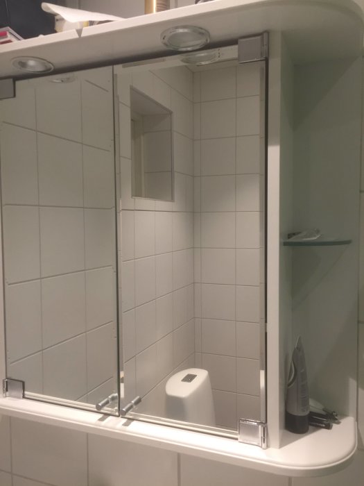 Badrumsskåp med spegeldörrar öppna, integrerade ledlampor ovanpå, en med saknat skyddsglas.