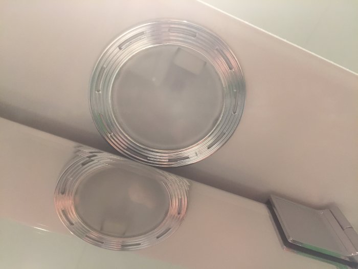 Två runda badrumslampor monterade på en skåpsida, en med och en utan skyddsglas.