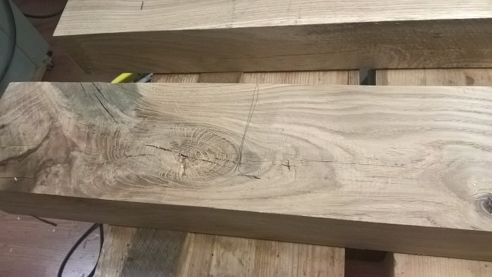 En stor träplanka med tydlig ådring, kvistar och längsgående sprickor ligger på ett arbetsbord.