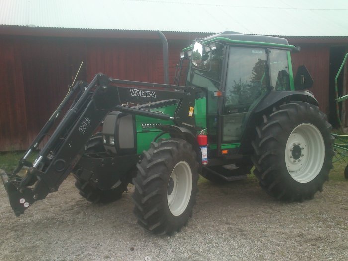 Grön Valtra traktor modell 800 med frontlastare parkerad framför en röd lada.