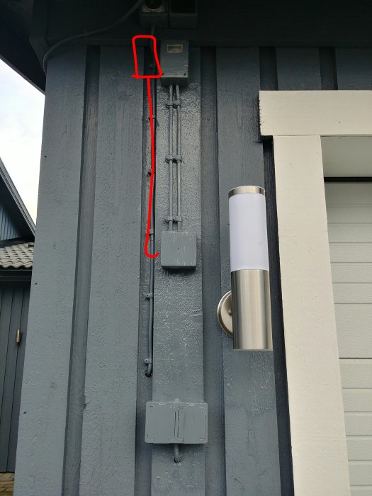 Målat elskåp och rör med markerad position där en kabel avlägsnats på en husvägg.