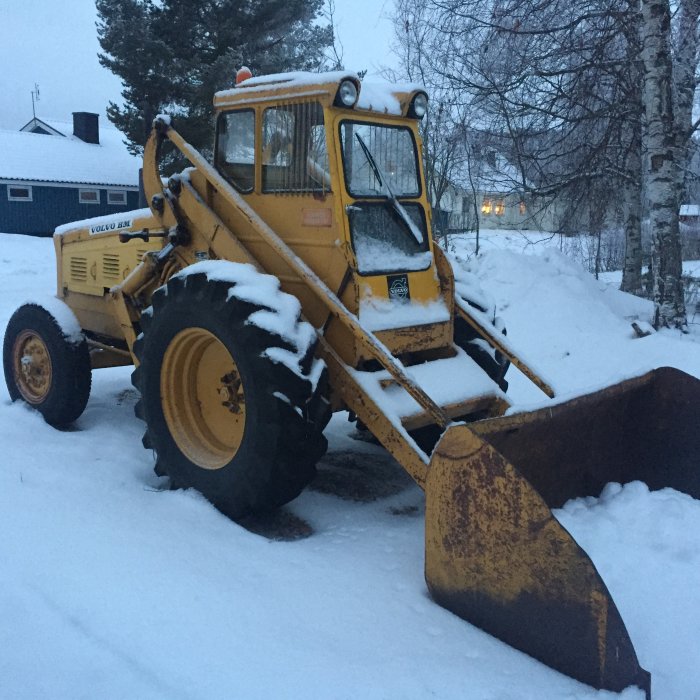 Gul Volvo BM baklastare täckt med snö parkerad utomhus under vintern.