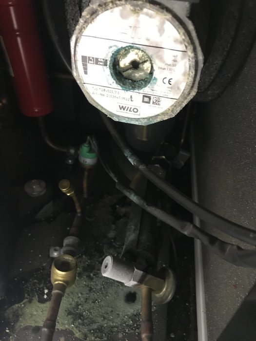 Oxiderad koppar syns på en cirkulationspump märkt WILO, omgiven av rör och kablar, tecken på läckage eller kondens.