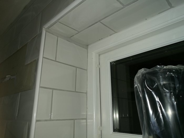 Ojämna fogar och kakel vid fönster i pågående badrumsrenovering.
