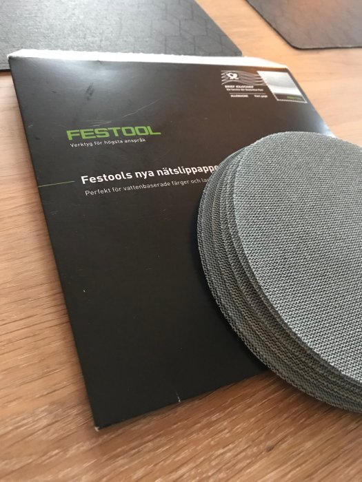 Festool broschyr för nät-sandpapper och en hög av gråa sandpappersskivor på ett träbord.