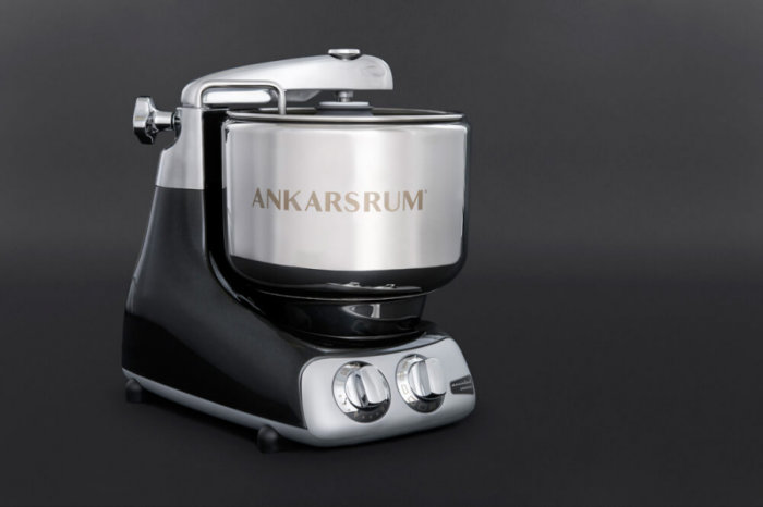 Svart Ankarsrum köksassistent med köttkvarnstillbehör mot en mörk bakgrund.