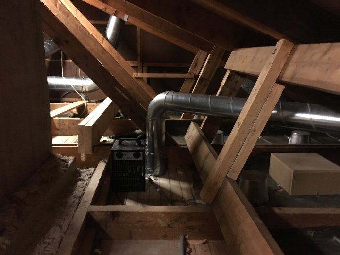 Bjälklag med synliga träkonstruktioner, elinstallation och ventilationsrör i ett ouisolerat vindsutrymme.