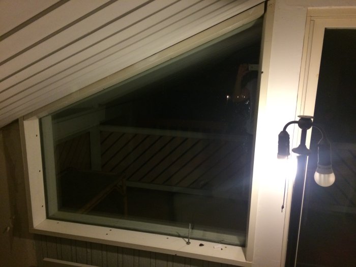 Ett loftfönster med klumpiga träbrädor som stöd och en utomhuslampa i förgrunden.