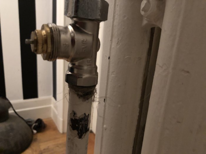 Mässingsventil på ett tvårörssystem för uppvärmning nära en vit vägg, med synlig mässingsmutter och termostatstift.