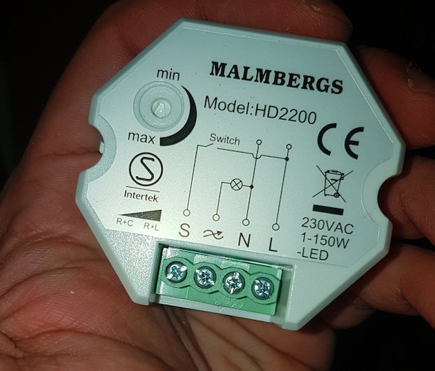 Hand håller en Malmbergs HD2200 dosdimmer med märkningar för anslutningar och justeringsratt för min-max.