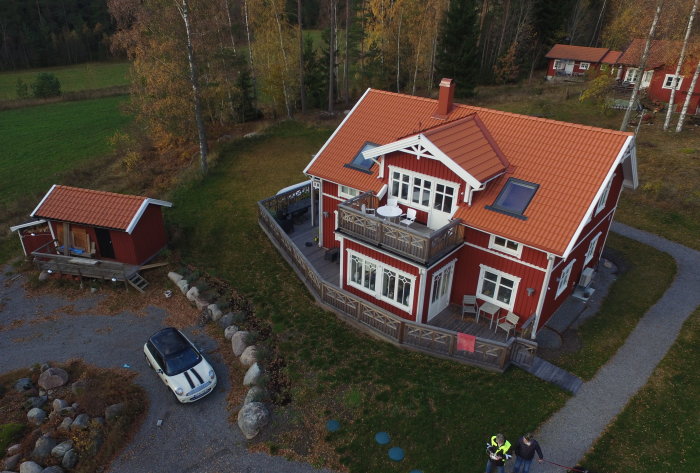 Rött hus med tegeltak och vita fönster, omgivet av natur, sedd ovanifrån.