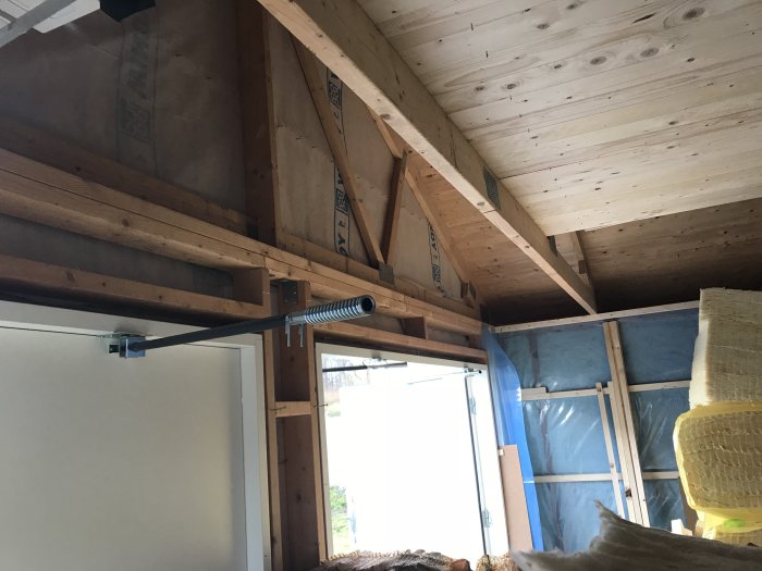 Interiörbild av ett garage under renovering som visar träbjälkar och en oavslutad takskjutport.