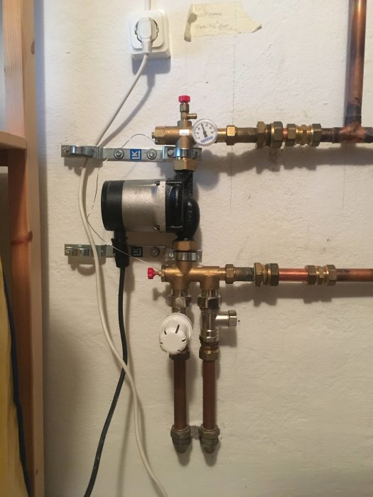 Golvvärmeinstallation med Grundfos pump och termostat, rör och manometer synliga.