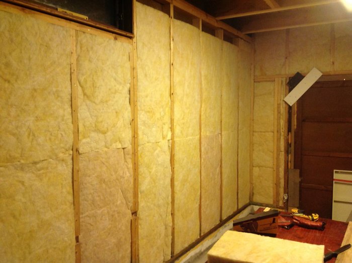 Isolerade väggar med mineralull i ett pågående renoveringsprojekt, med verktyg synliga.
